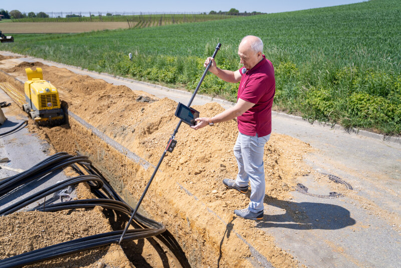 Mann mit GNSS-Sensor in der Hand steht im Graben