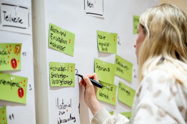 Eine Person notiert bei einem Workshop Prioritäten auf einer Wand mit grünen Klebezetteln zum Themena Hochwasserschutzes. 
